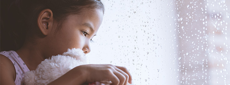 child holding teddy bear looking out window during a storm as family prepares for a hurricane