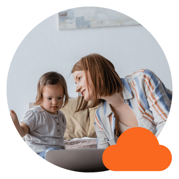A mother and her young daughter sit together at home, looking at a laptop screen with curiosity and focus.