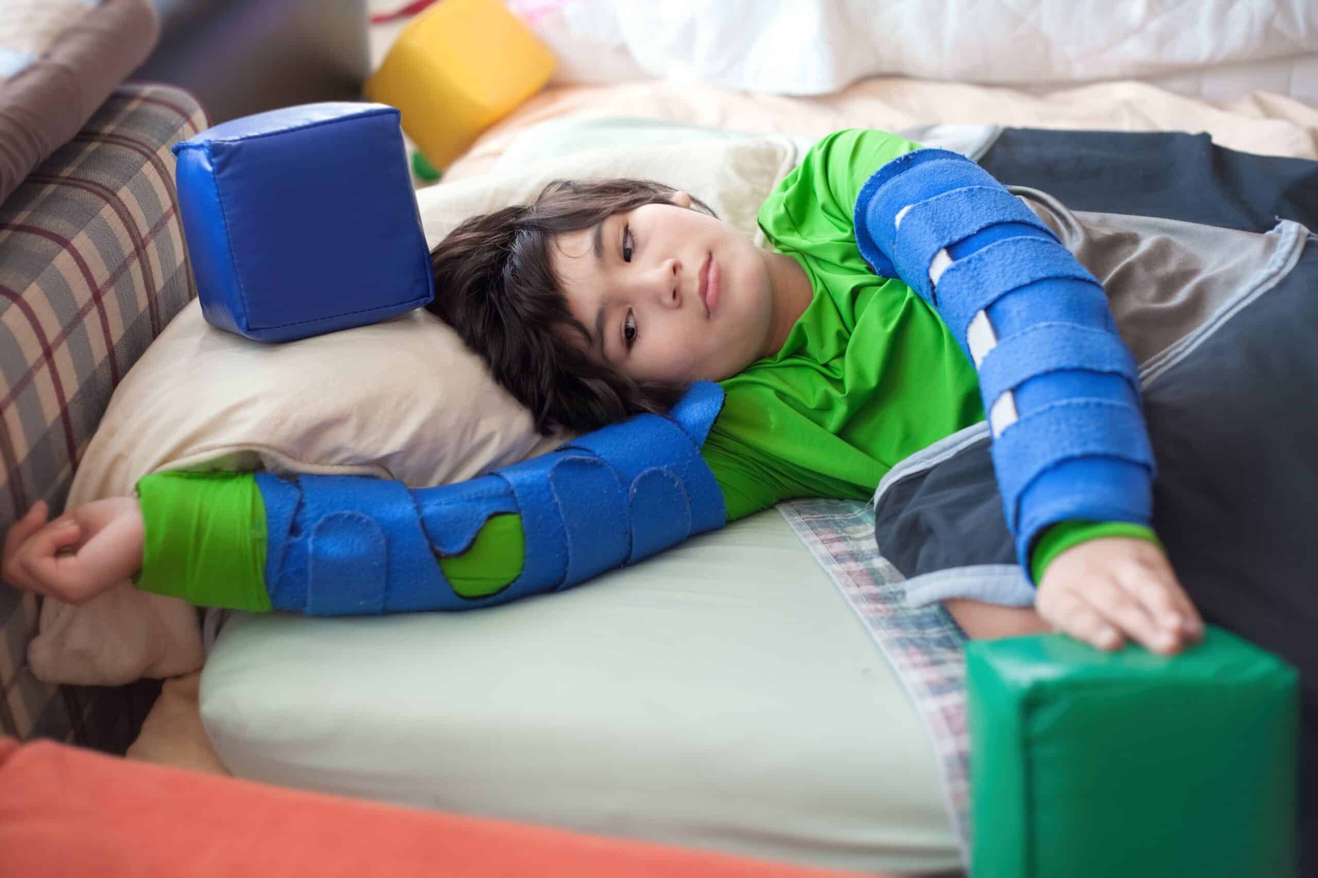 Child resting in a padded safety bed with blue arm supports and surrounding cushions.